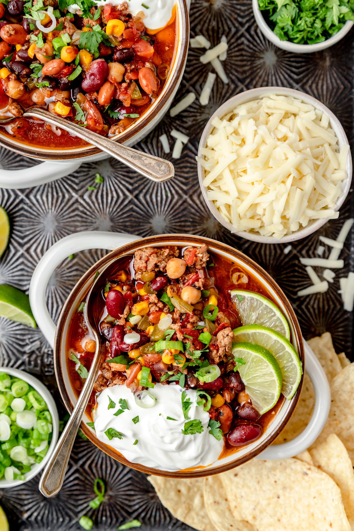 Two servings of colorful slow cooker chili in bowls with sour cream and lime slices.