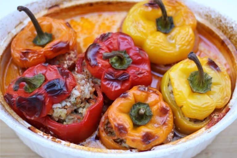 Baked bell peppers stuffed with seasoned ground beef, rice, and carrots in a baking dish.