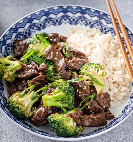 Beef and broccoli with rice on blue and white plate with chopsticks