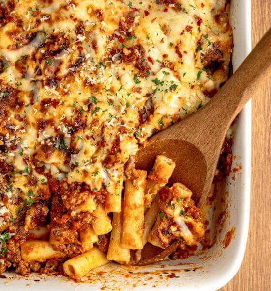 Baked ziti in white casserole dish with wooden spoon