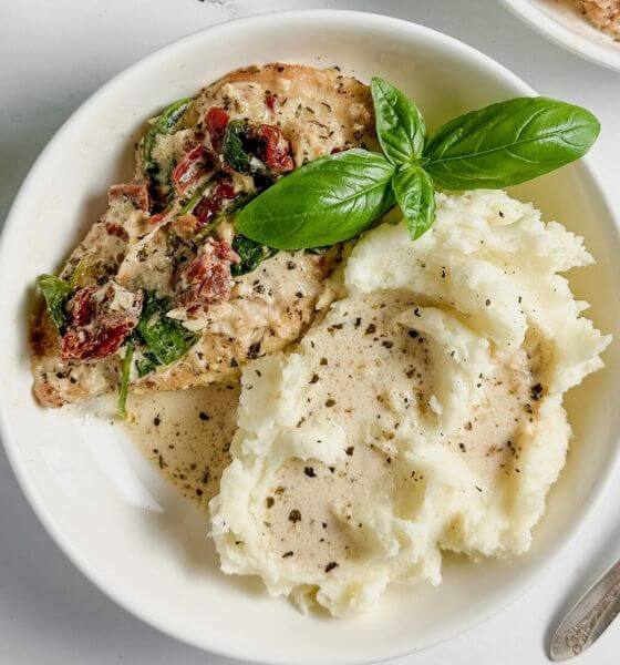 Tuscan chicken and mashed potatoes on white plate