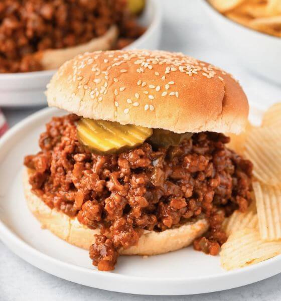 Sloppy joe on white plate with a pickle