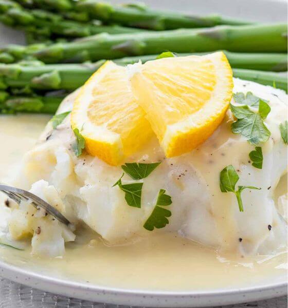 White fish with lemon slice on white plate with asparagus
